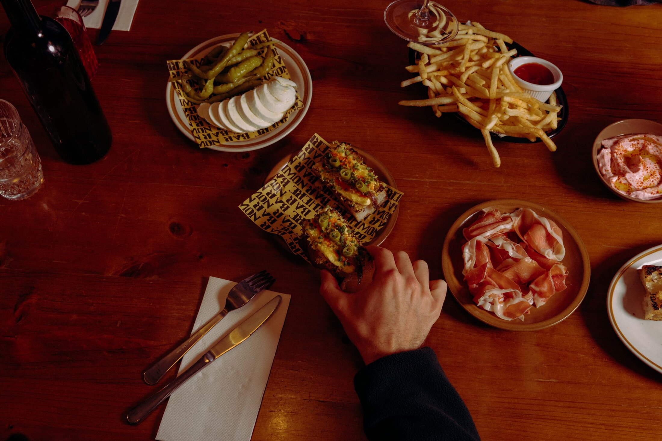 Hands reaching across a table of shared plates at Nowhere Bar