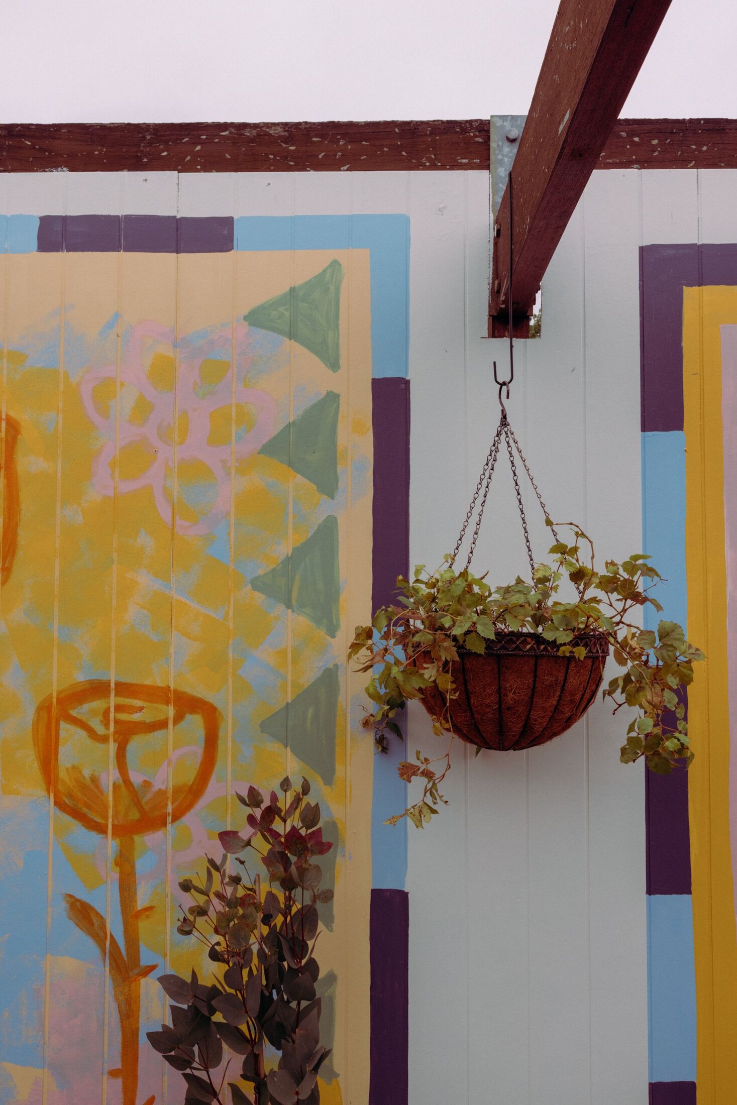 A corner of Nowhere's hand-painted mural, with a hanging plant against the colour